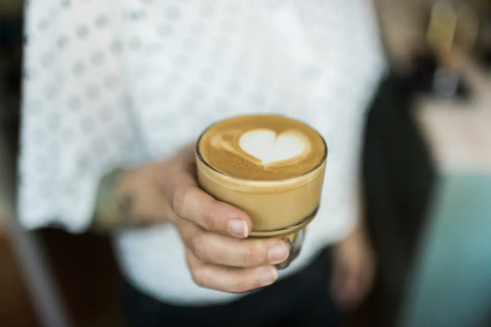 Frau hält ein Glas mit Kaffee, Kaffeschaum formt ein Herz
